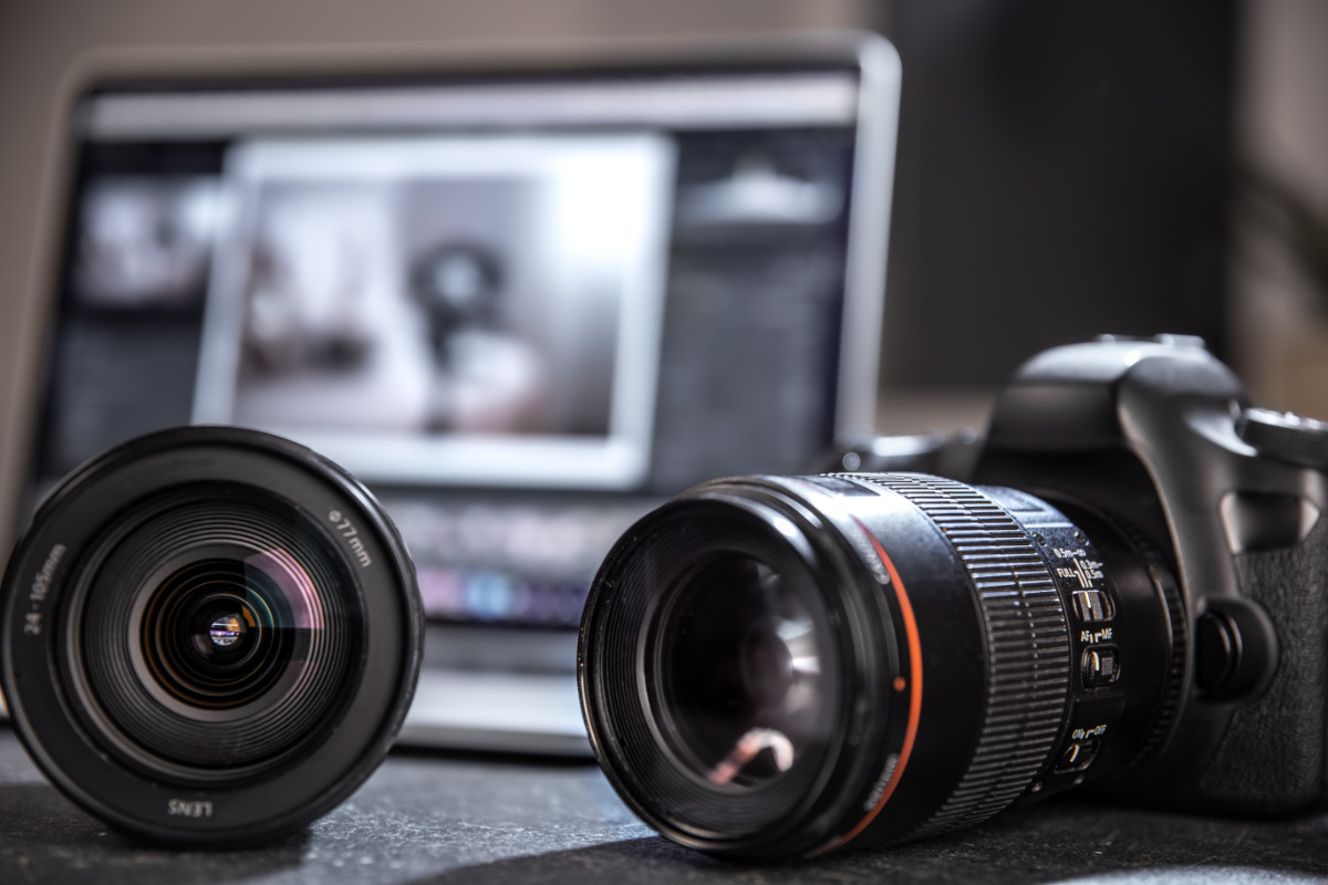 Close up of a professional digital camera and lens on the desktop of a photographer with a laptop.